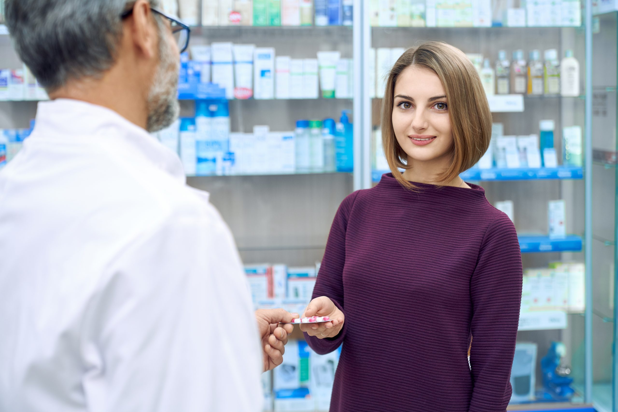Portrait of satisfied female customer buying medicaments in drugstore and looking at camera. Crop of unrecognizable mature pharmacist offering woman medical products, giving blister pack of pills.